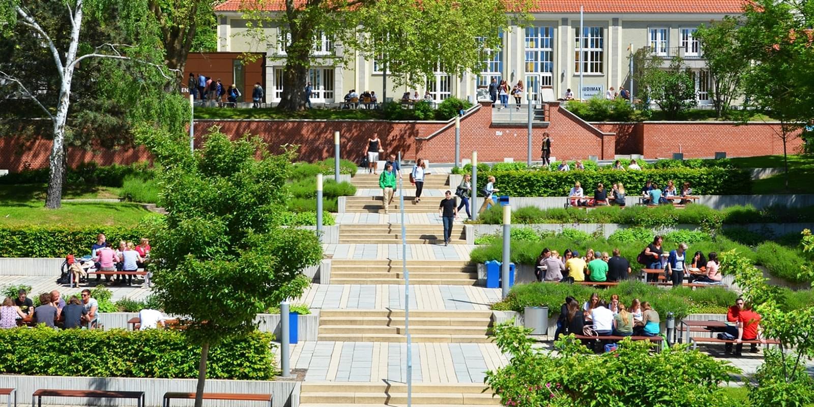 Grüner Campus der Hochschule - große Treppe zum Audimax - Studierende sitzen an Tischen