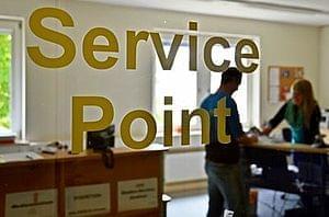 Glastür des Servie Points - Aufschrift Service Point in Gelb. Dahinter das Büro, eine Person steht im Raum.