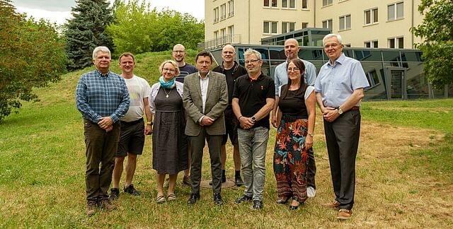 Das Team der IAE steht auf dem grünen Campus, im Hintergrund die Bibliothek der Hochschule