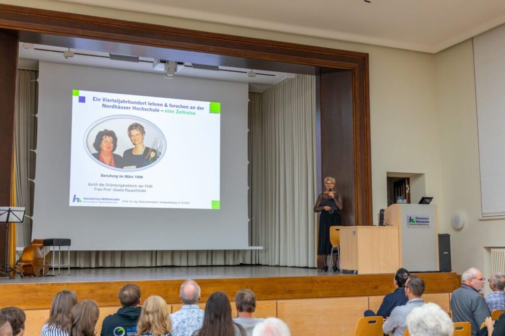 Professorin auf Bühne hält Vortrag vor Zuhörerschaft