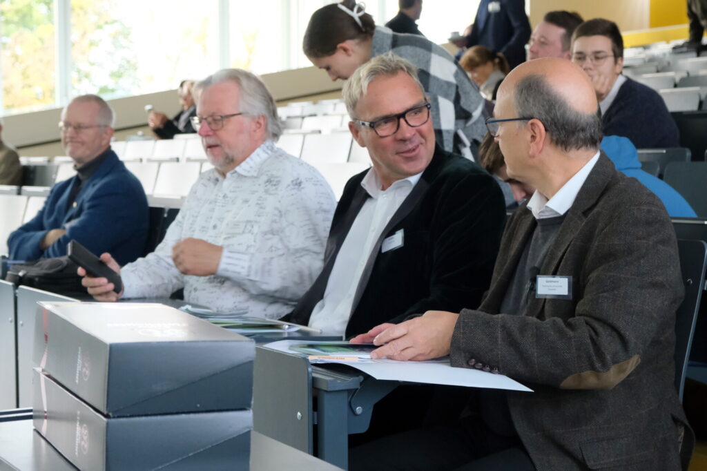 Zwei Männer im Publikum lächeln, während sie auf ein Tablet schauen und miteinander sprechen.