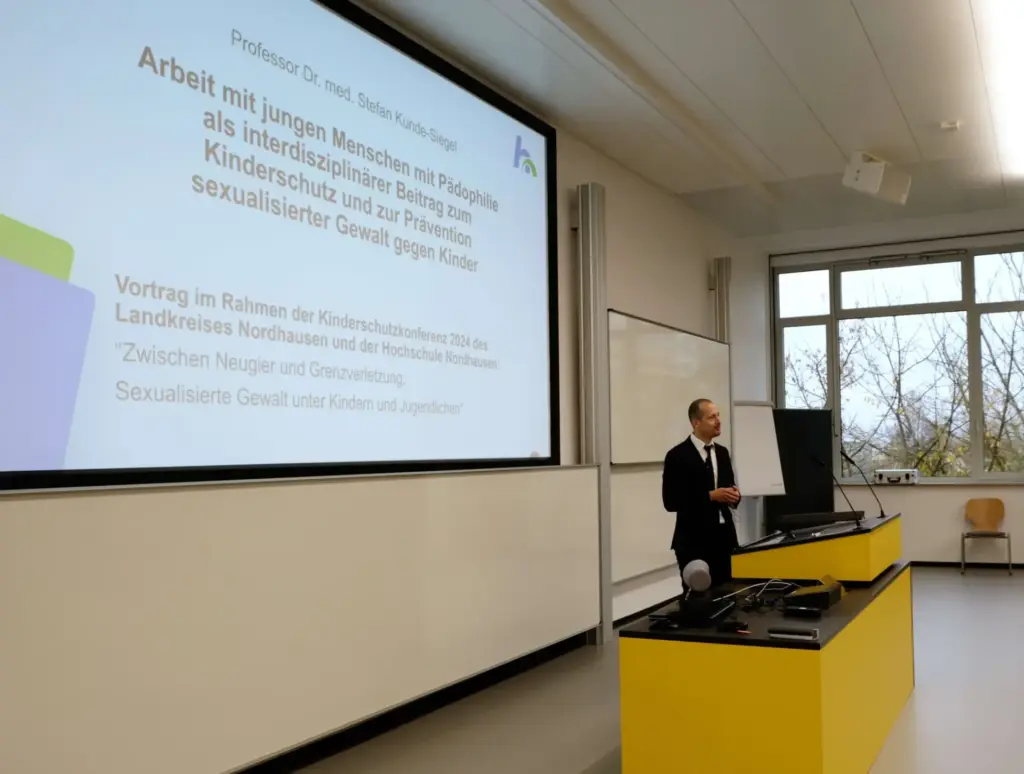 Prof. Kunde-Siegel präsentiert vor einer Folie mit dem Titel „Arbeit mit jungen Menschen mit Pädophilie als interdisziplinärer Beitrag zum Kinderschutz und zur Prävention sexualisierter Gewalt gegen Kinder“. Der Vortrag findet im Rahmen der Kinderschutzkonferenz 2024 statt.