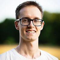 Portrait Maurice Töpfer - ein junger Mann mit kurzen dunklen Haaren. Er trägt eine Brille und ein weißes T-Shirt.